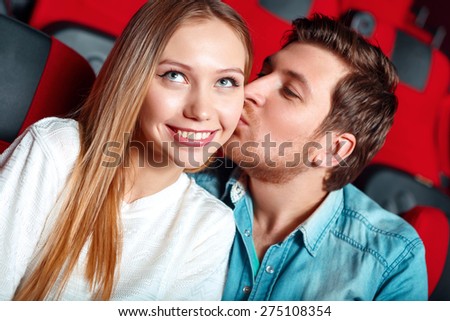 Give me kiss. Young man giving kiss cheek of young pretty woman in cinema.