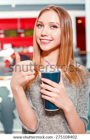 It is cool. Young-looking woman standing in hall before watching film in cinema with coke and showing class.