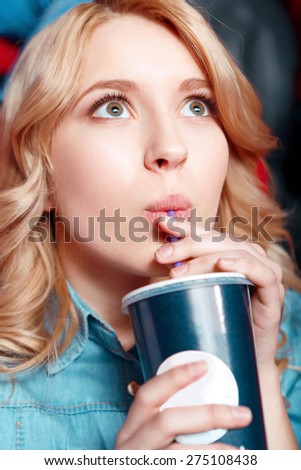 Rapturous girl. Young blond woman enthusiastically watching film and drinking coke in cinema