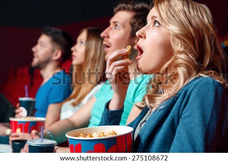 Emotional film. Excited blond woman eating popcorn emotionaly in cinema near other viewer.
