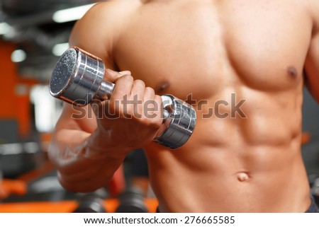 Continuing working out. Muscular handsome weightlifter working out with dumbbells in sport gym.