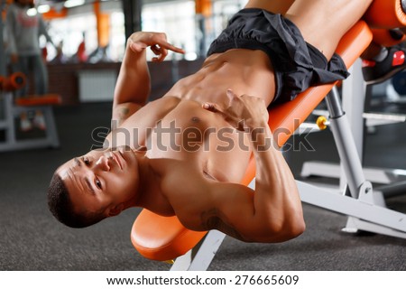 Upside down. Muscular handsome man lying upside down and pointing on his press.