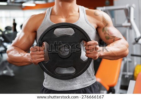 Total focusing. Portrait of handsome muscular powerlifter with weight disk in his hands on sport gym club.