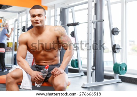 Having relax. Sportive young man sitting with bottle and towel in sport gym.
