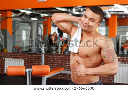Thumbs up. Young muscular man wiping himself with towel in sport gym and pointing thumbs up.