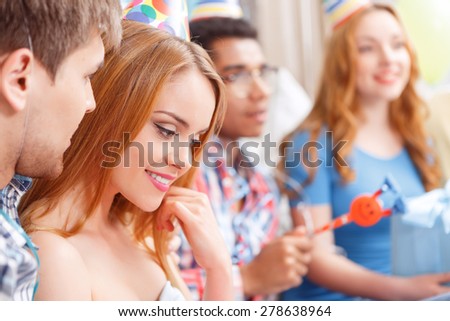 Birthday party. Side view of two young beautiful blond girls smiling and their boy friends blowing at the party horn selected focus