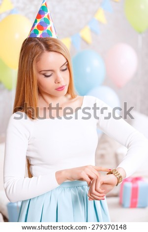 Friends are late. Young beautiful blond girl wearing cone cap looking at her watches because her guests are late for the birthday party