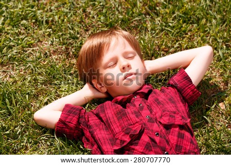 Sweet dreams. Little boy lying on grass with hands behind his head and sleeping.