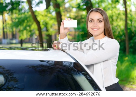 Look at this. Attractive young woman leaning on white new car and showing card