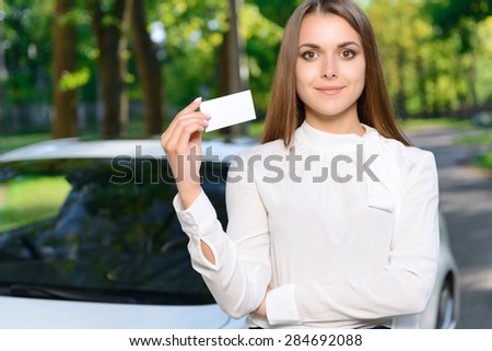 Showing off. Portrait of youthful beautiful lady standing in front of white new car and holding card.