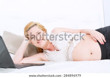 Cheerful mind. Pregnant young woman touching her belly and smiling while having rest on the couch.