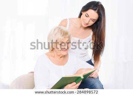 Reading together. Two women of different ages sitting on armchair and reading book.
