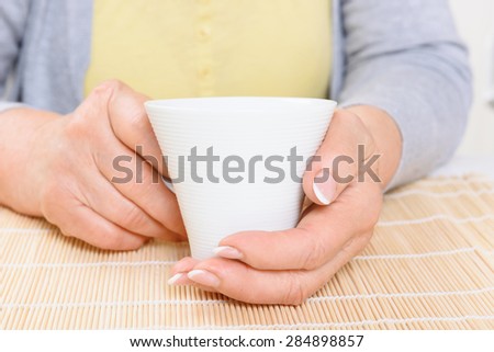 Taking rest. Portrait of white cup held by old lady in kitchen