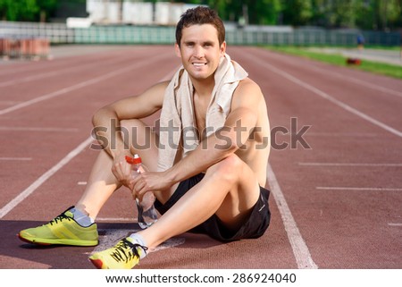 After exercising. Attractive young topless man sitting on floor and having rest