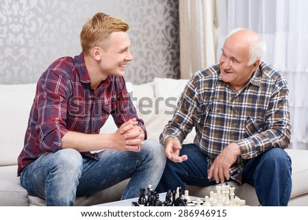 Conversation during game. Grandfather and grandson sitting on couch together  and having conversation while playing chess.