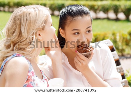 Telling secrets.  Young blond-haired girl telling secret to her friend with cupcake.