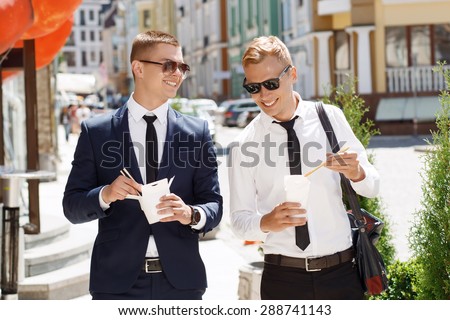 Busy men. Young attractive men going through street and keeping Chinese fast food.