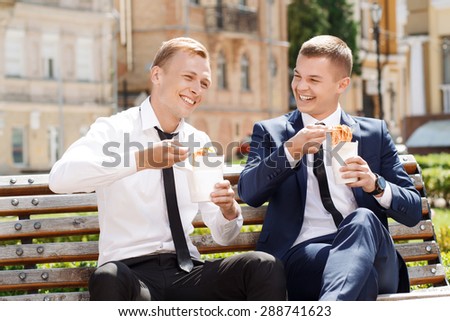 Sweet conversation. Two young handsome men sitting on bench and eating Chinese noodles while having conversation.
