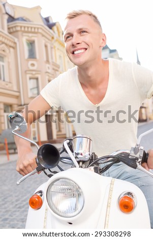 Sincere smile. Attractive happy man driving scooter on street.