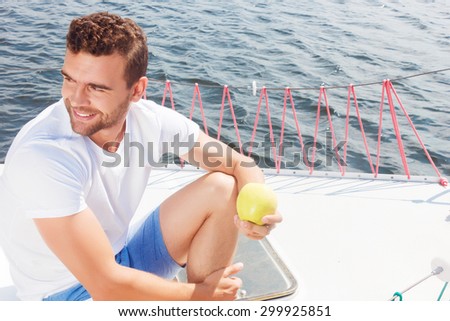 Feeling healthy and wealthy.  Vivacious handsome  man holding apple while sitting on the deck