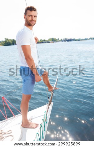 Follow wind.  Upbeat smiling man holding rope and standing on the yacht deck while expressing joy.
