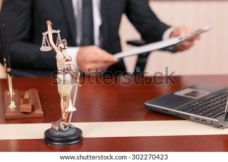 Law and equility. True lawyer sitting at the table and holding papers with statue of justice on forefront