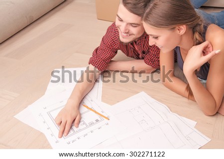 Look here. Top view of smiling pleasant young couple lying on the floor and making plan together while evincing joy.