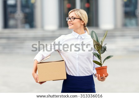 Ready to work. Pleasant vivacious businesswoman holding box and flower pot while going to work