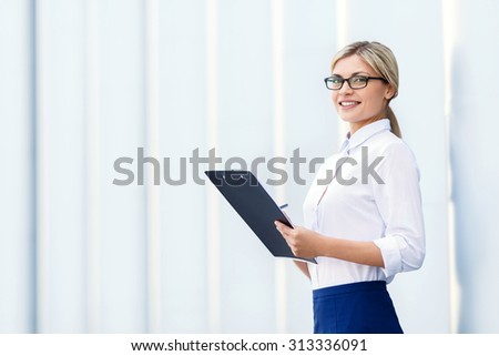 Way to success. Vivacious delighted beautiful businesswoman holding folder and reveling in her work while standing near office building