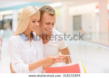Our buyings. Positive upbeat young couple opening package and looking in it while going shopping together.