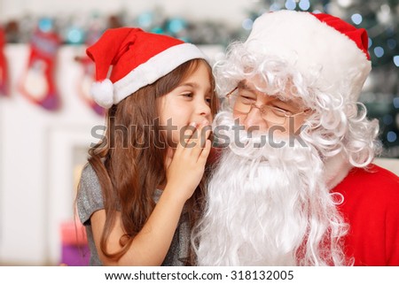 Let my dreams come true. Nice little girl holding her hand near face and talking with Santa while waiting for holiday