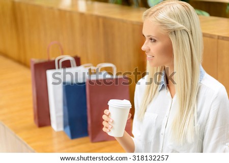 In harmony with mind. Nice beautiful positive woman drinking coffee and relaxing on the bench while making shopping.