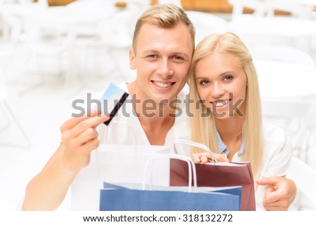 It is my card. Nice blissful young couple sitting in the cafe and holding packages while resting after shopping