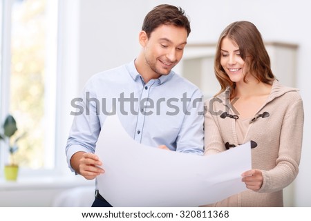 Involved in work. Cheerful handsome upbeat realtor holding plan of the house while presenting it to his client