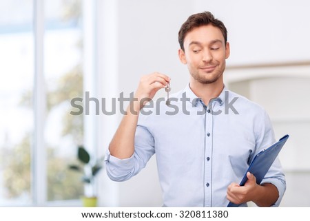 Will make you happy. Cheerful pleasant professional realtor holding key from new flat  and keeping folder while being involved in work