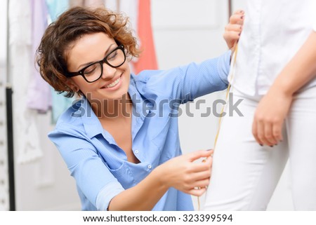 Do it precise. Pleasant overjoyed young designer holding measure tape and measuring her client while evincing gladness