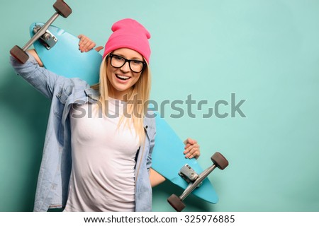 Revel in skating. Cheerful agreeable young girl holding the skateboard and expressing positivity while standing isolated on blue background