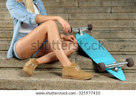 Take a minute for rest. Close up of active young girl sitting on the footsteps near her skateboard while having rest