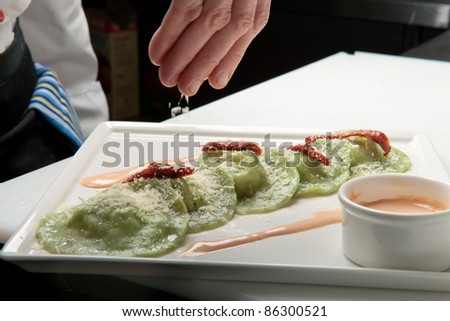 A chief cook masterly preparing delicious green ravioli with pesto sauce at the kitchen decorating raviolli with parmesan