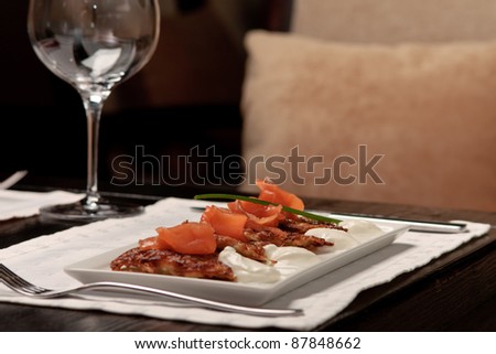 Crispy potato pancakes decorated with salmon and sour cream being served by a waiter