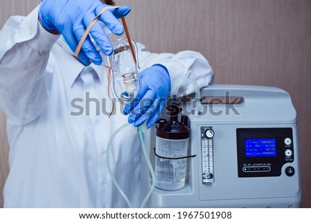 Hands in medical gloves hold out an oxygen mask against the background of the oxygen generator concentrator  to deliver at low lung oxygen saturation for Covid-19 pneumonia. Focus on oxygen mask Photo stock © 