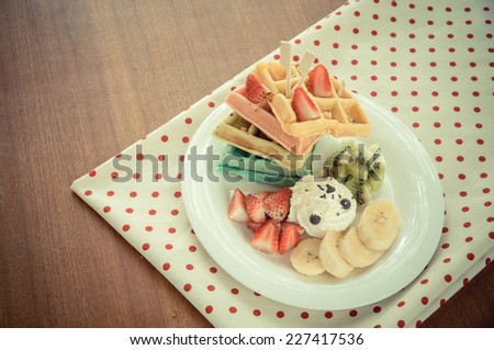 Colorful waffle and fruit on wood table with cloths.