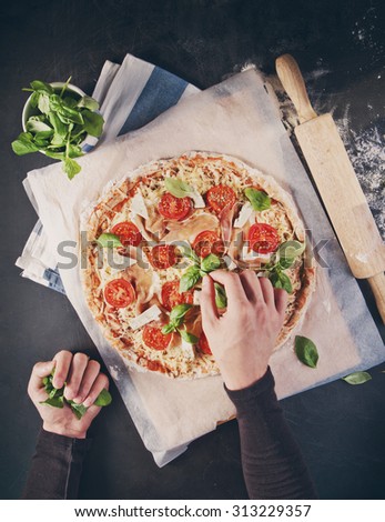 Hands of baker adding ingredients into pizza during pizza preparation at kitchen