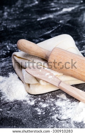 Classic wooden rolling pin with freshly prepared dough and dusting of flour on black background