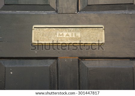 Front door golden brass metal mail slot in a black door