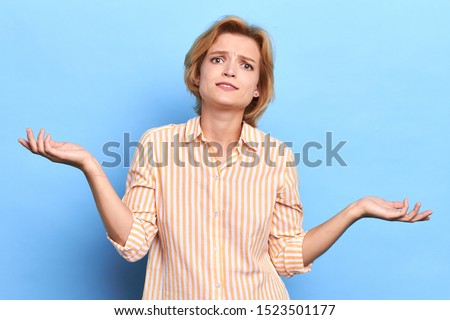 puzzled unhappy young woman shrugging her shoulders, girl doen't know what to do. body language, close up portrait, isolated blue background, studio shot Stockfoto © 