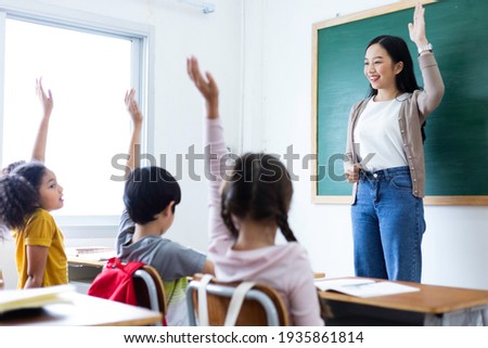 Diversity of elementary school students raise their hands to answer teacher questions in class room. Back to school concept