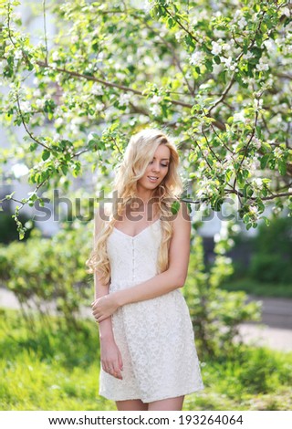 Lovely girl in white dress in spring garden, enjoying warm sunny day, beautiful blonde on nature