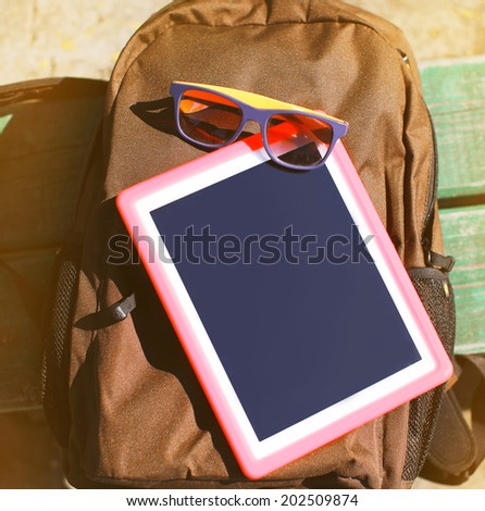 Fashion summer hipster concept, screen tablet pc and sunglasses on the backpack, top view