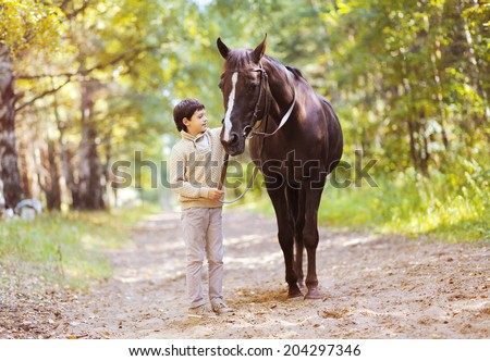 Cute teenager boy and horse in the forest in summer day